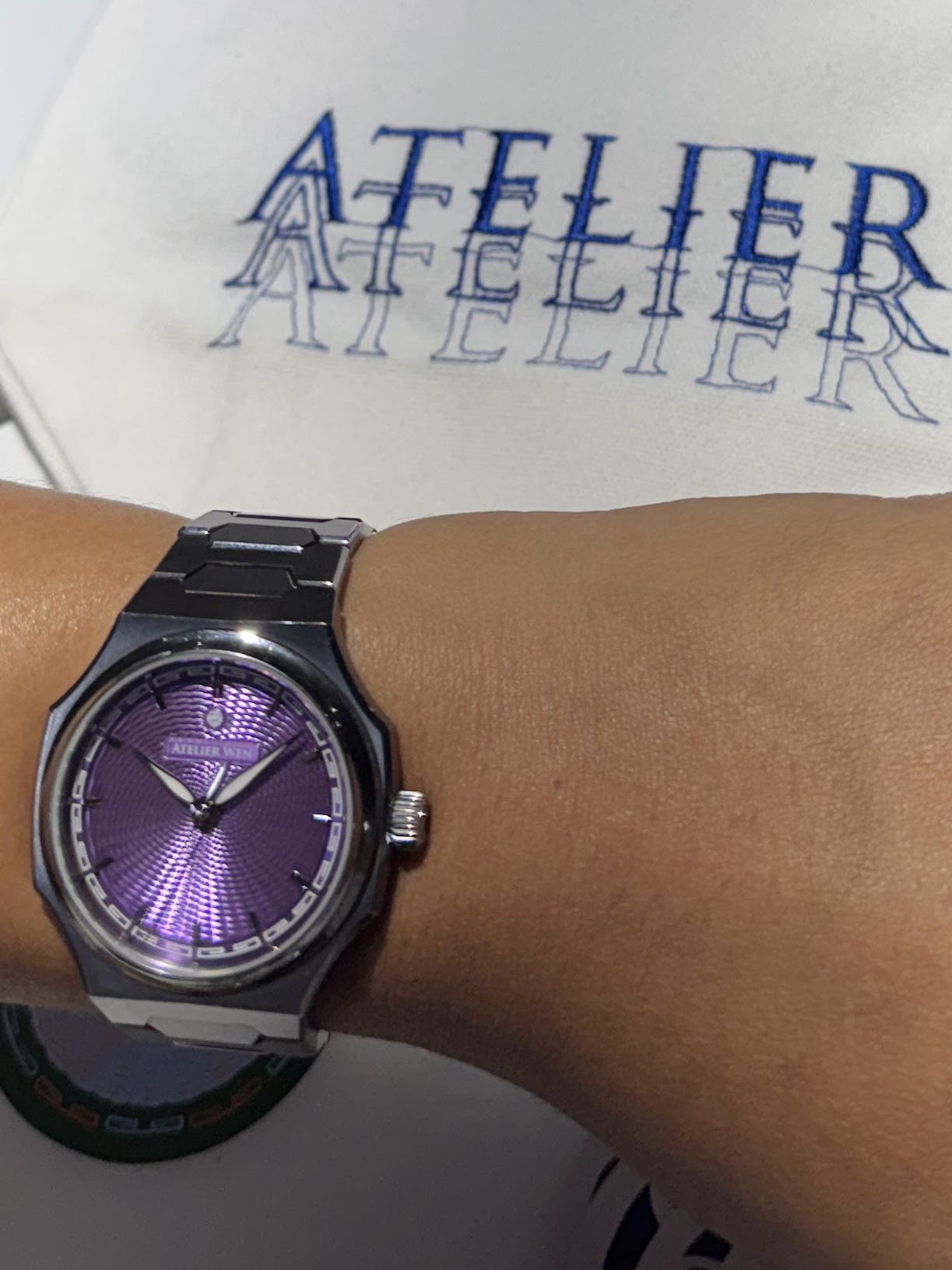 Close-up of a wrist wearing an Atelier Wen watch with a purple guilloché dial, set against a white background featuring the brand name Atelier.